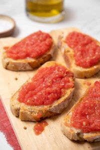 Four slices of toasted rustic bread topped with fresh grated tomato and salt, served on a wooden board.